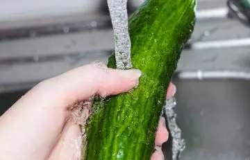 Close up of hands washing cucumber in the kitchen sink under running water