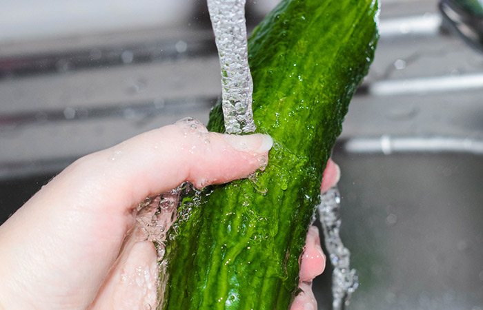 Close up of hands washing cucumber in the kitchen sink under running water