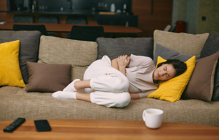 Woman clutching her stomach and lying on the couch because of digestive pain