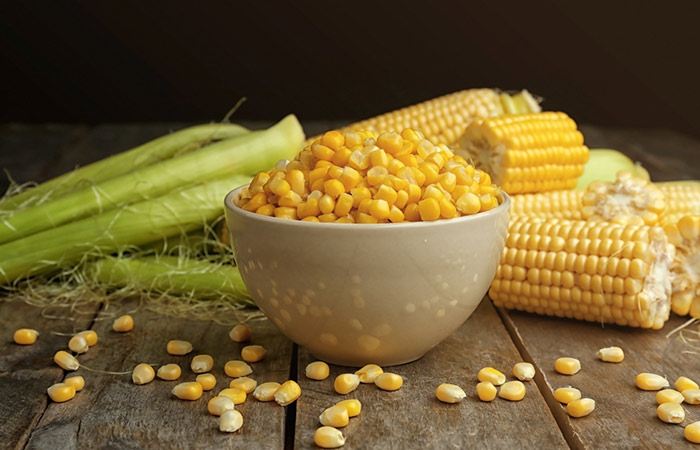 A bowl of corn kernals against the backdrop of corn cobs