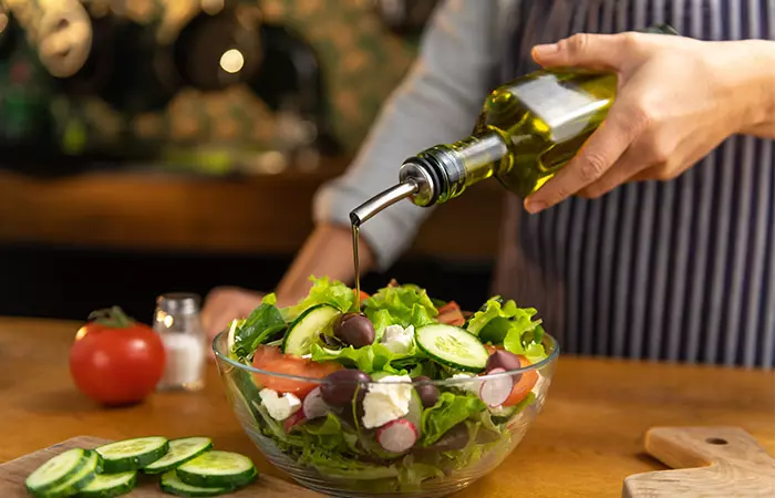 Chef pouring olive oil into a bowl of caesar salad because of it's healthy fat content