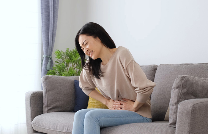 Woman with stomach ache sitting on a sofa in the living room. 