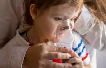 Woman helping son with a nebulizer at home due to breathing difficulties
