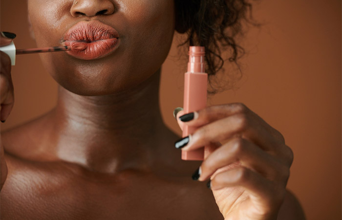 Close up of a woman with dark skin applying peach lipstick