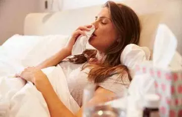 Woman lays in bed with a runny nose due to cold and postnasal drip