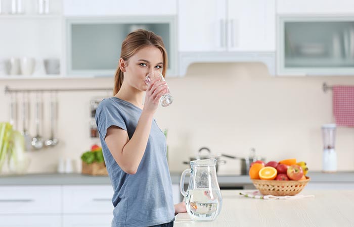 Young woman drinking pure water from glass in kitchen.
