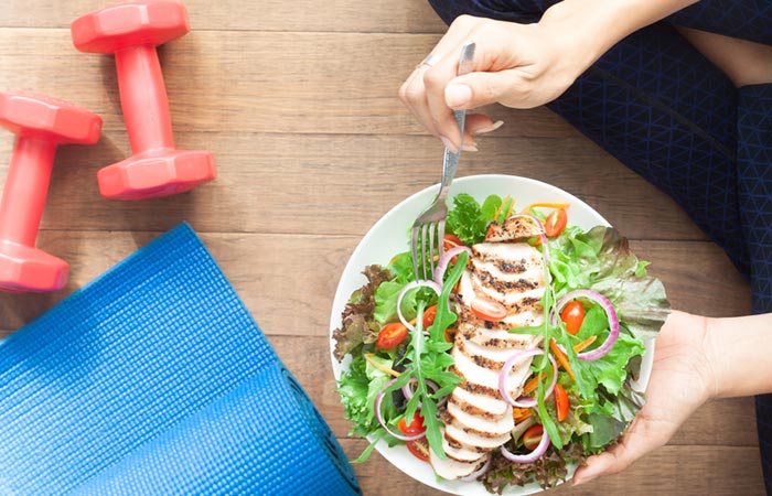 A healthy woman eating healthy salad with dumbbells and yoga mat beside