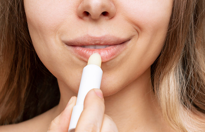 A closeup of a woman applying lip primer to prevent lipstick transferring.