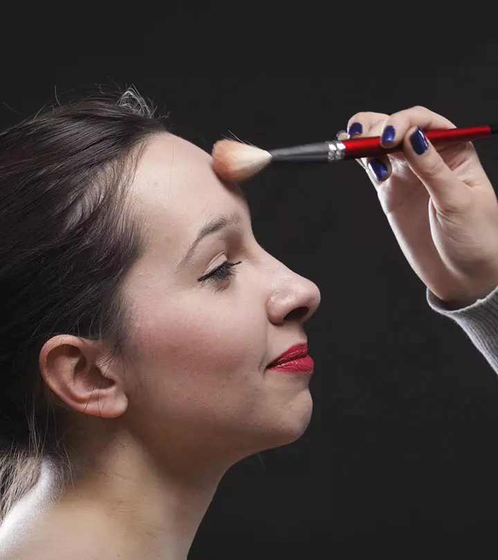 A woman is applying bronzer on her face