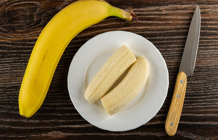 Unpeeled banana, halves of peeled banana in white plate