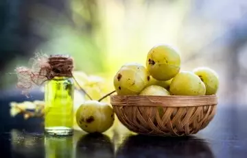 A small bottle of amla oil and a basket of raw amla for hair 