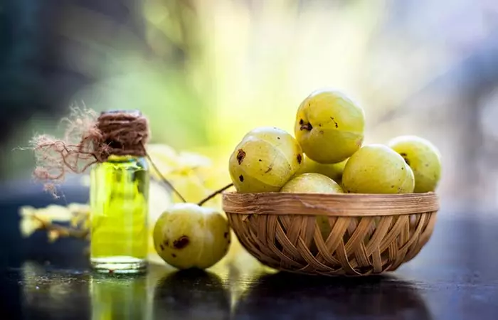 A small bottle of amla oil and a basket of raw amla for hair 