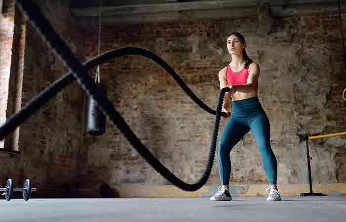 A woman engaging in battle rope HIIT workout to tone upper back