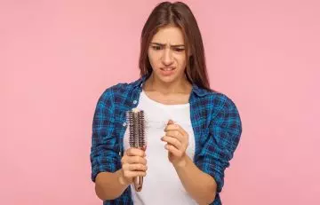 Beautiful woman looking at brush with hair stuck in it