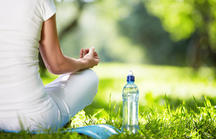Woman meditates with a bottle of water beside her as part of her weight loss and detox routine