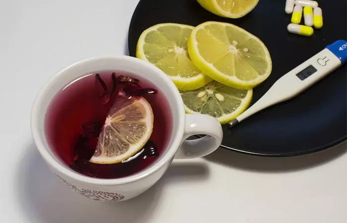 A cup of hibiscus tea with lemon slices and a few antibiotic tablets and thermometer for viral fever and infections
