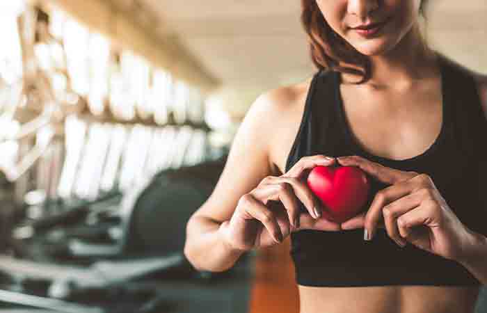 Woman in gym holding model of a heart symbol against her chest