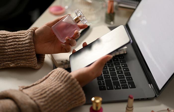 Woman at her work desk holding a bottle of perfume and a phone