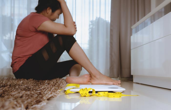 Unhappy woman sitting beside a weight scale