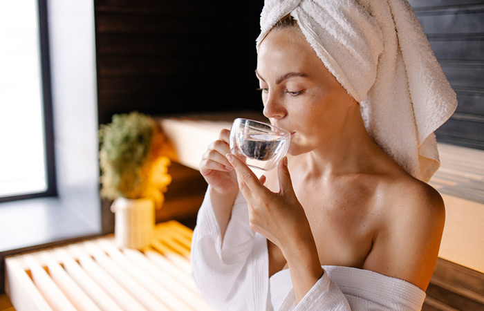 Woman drinking a glass of water for hydration after a steam bath for weight loss