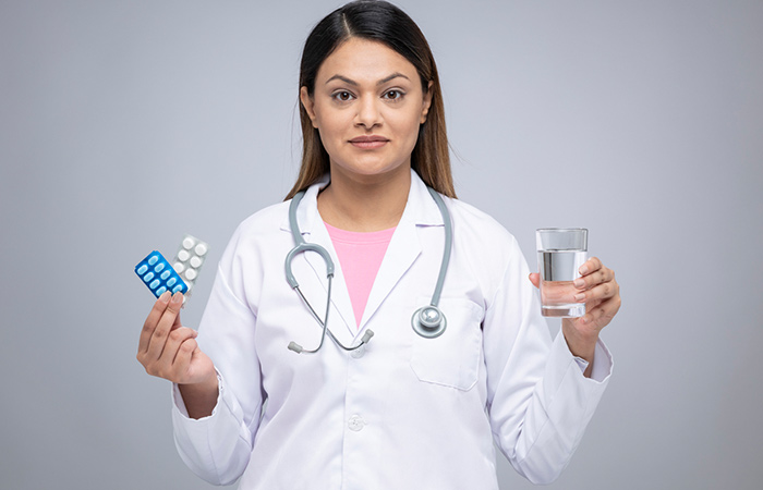 A doctor holding aspirin tablets and a glass of water.