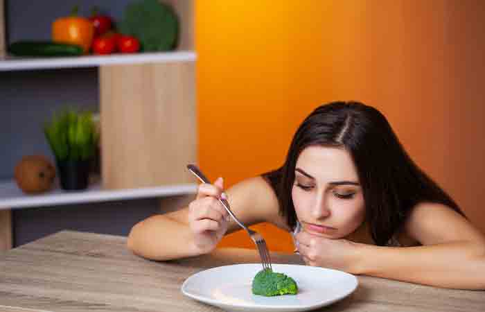 Woman on a warrior diet sadly plays with the single brocoli on her plate as she is upset with the low quantity of food