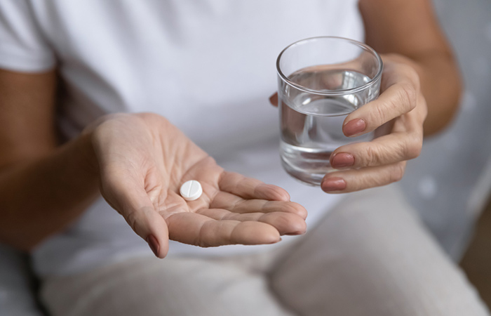 Close up of a woman holding an aspirin tablet and a glass of water.