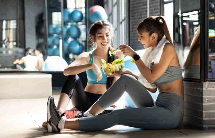 Two women taking a break after an intense workout session to enjoy their portioned warrior diet meal