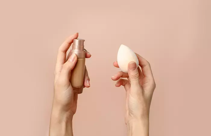 Close up of a woman's hands holding a concealer and a makeup sponge to cover the varicose veins