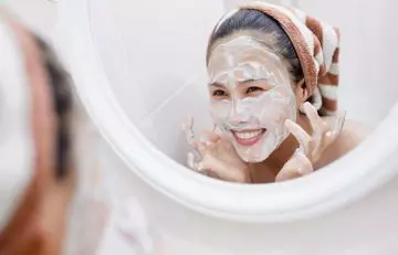 A woman smiling at her reflection after applying yogurt mask.