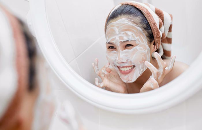 A woman smiling at her reflection after applying yogurt mask.