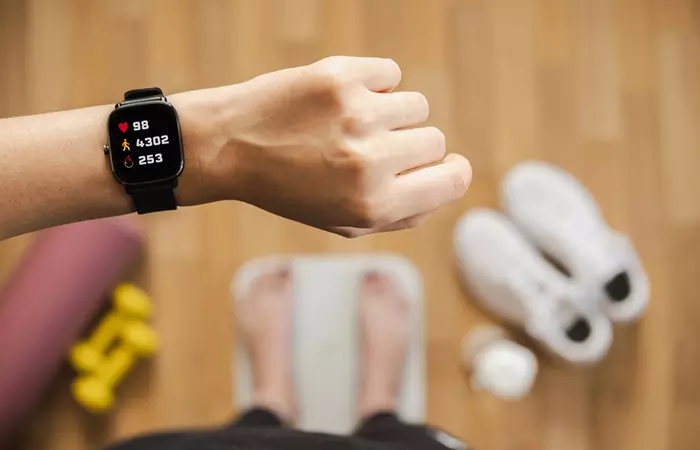 Close up of a fitness tracker on woman's hand displaying heart rate, steps count and burnt calories while standing on scales.