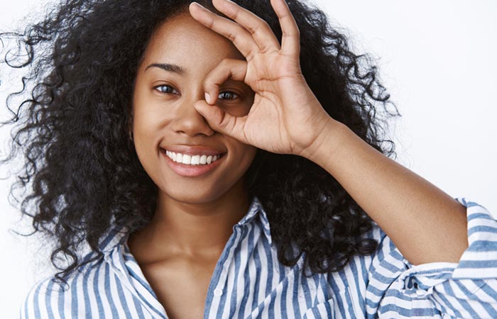 A woman is smiling and showing zero dark circles by making a hand gesture.