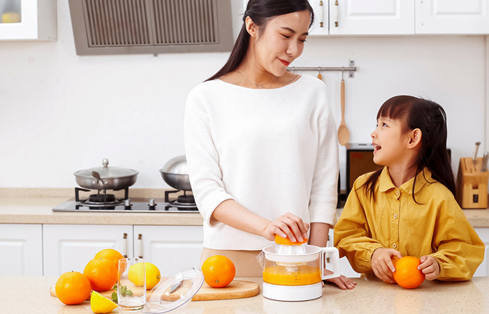 Woman making fresh orange juice with her little daughter
