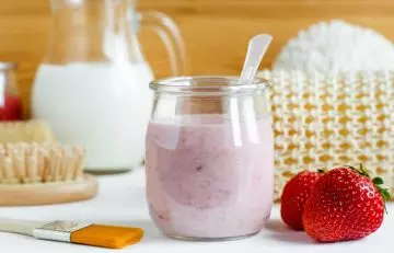 A jar of strawberry yogurt can be seen with a brush lying on the table.