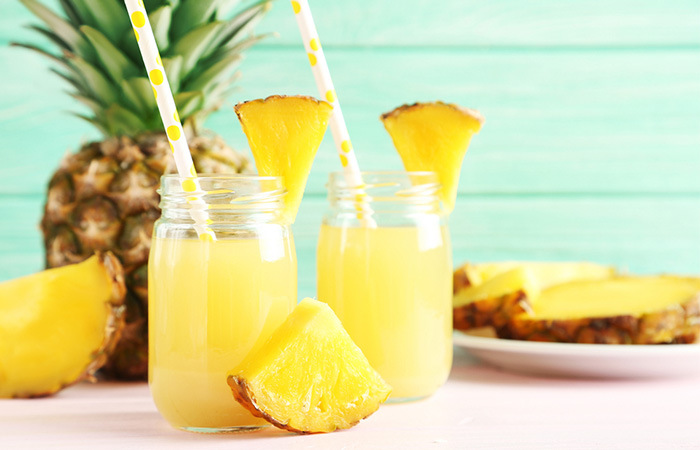 Two mason jar glasses of pineapple juice with pineapple pieces