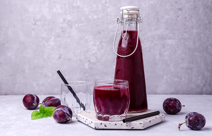 A glass and bottle of prune juice with prune fruits