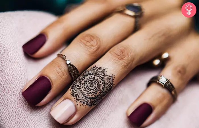 A minimalist mandala tattoo near the fingernail of the ring finger