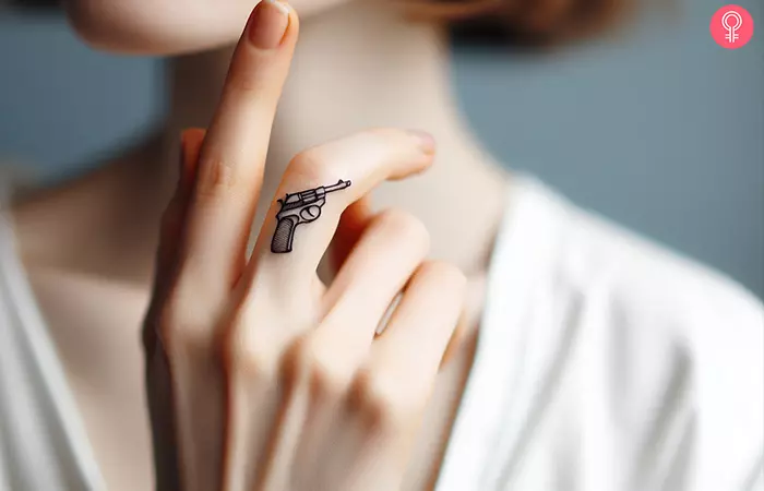 A minimalist revolver tattoo on the base of the middle finger