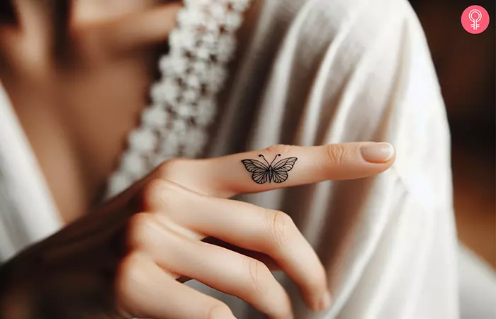 A tiny butterfly tattoo with open wings on the side of the index finger