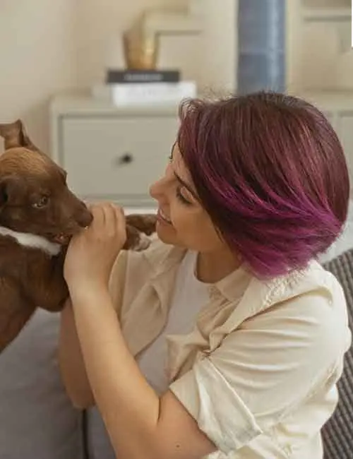 Woman with deep burgundy hair and purple highlights playing with a puppy