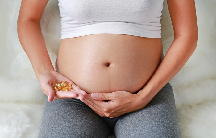 Pregnant woman holding a handful of fish oil pills near her belly