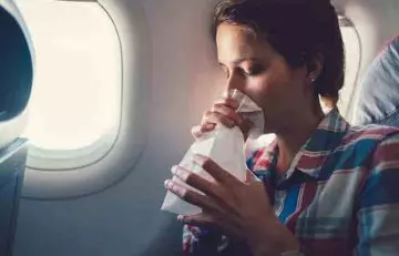 Woman holding a vomiting bag in her airplane seat as she experiences nausea as a side effect