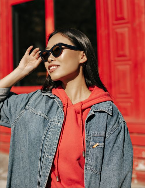 woman posing in jean jacket and hoodie with sunglasses