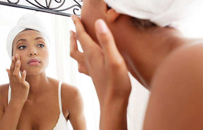 Woman looking at the mirror, hydrating her skin after cleansing