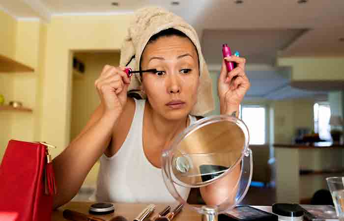 Woman in towel-wrapped hair applying mascara