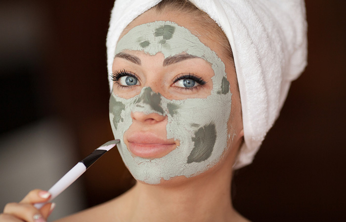 Woman applying bentonite clay mask on face