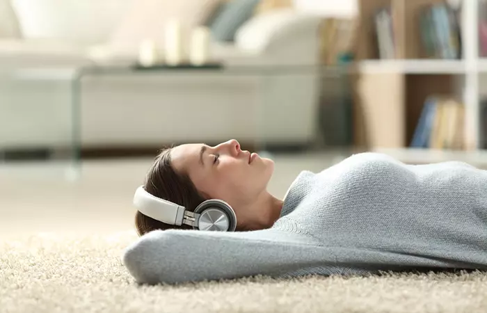 Woman with headphones on sleeps on carpeted floor with hands under her head for support