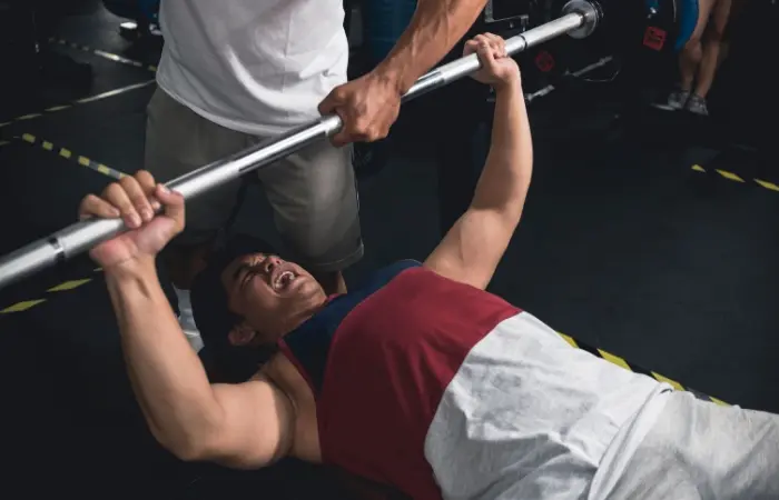 A man grunting while doing bench press in a gym