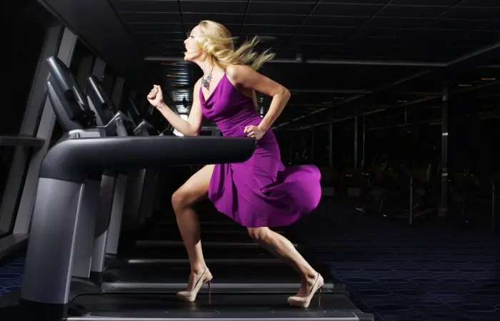 A woman in a dress running on a tredmill in a gym